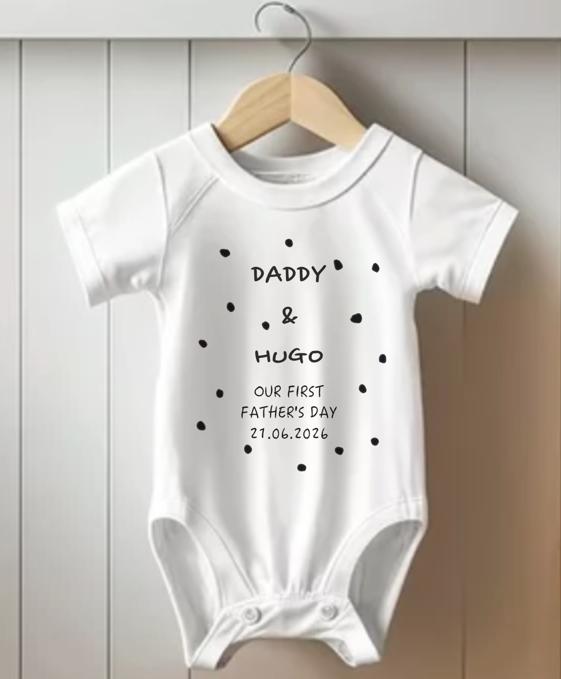 White baby onesie with text on a wooden hanger against a light wooden panel background