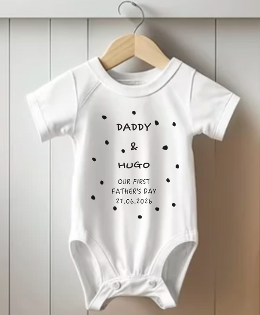 White baby onesie with text on a wooden hanger against a light wooden panel background